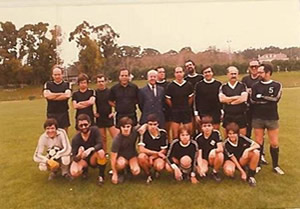 Grupo de jogadores de râguebi posados num campo relvado, vestidos maioritariamente de preto, em fotografia de equipa.